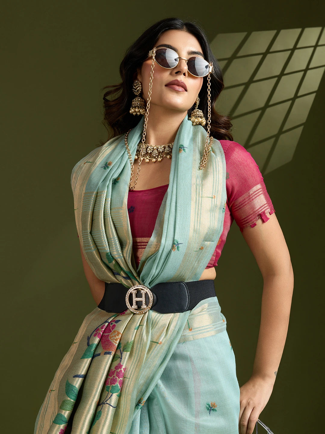 Woman in traditional outfit with sunglasses and jewelry against a green background