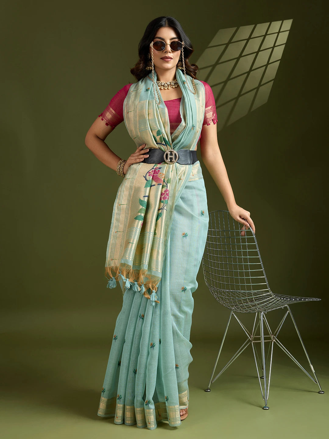 Woman in a light blue saree with a floral blouse standing against a green background
