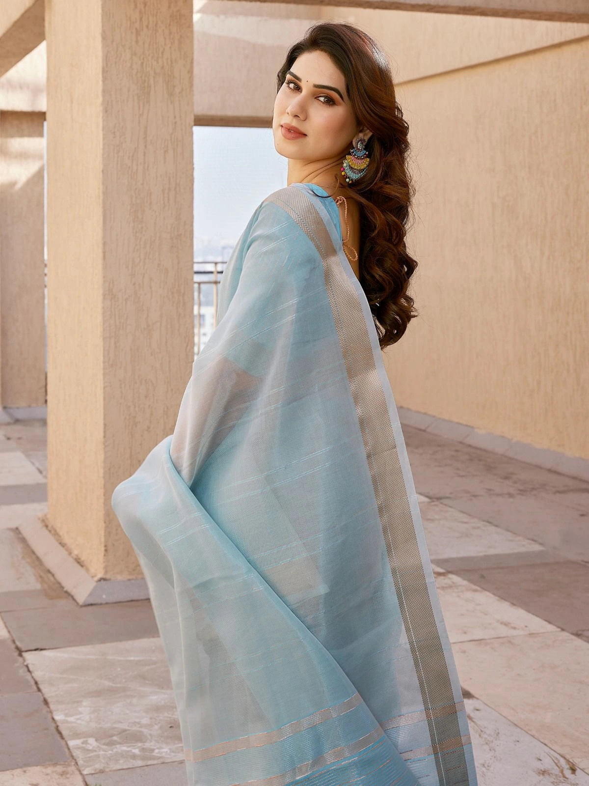 Woman in a light blue saree standing in an outdoor setting with columns.