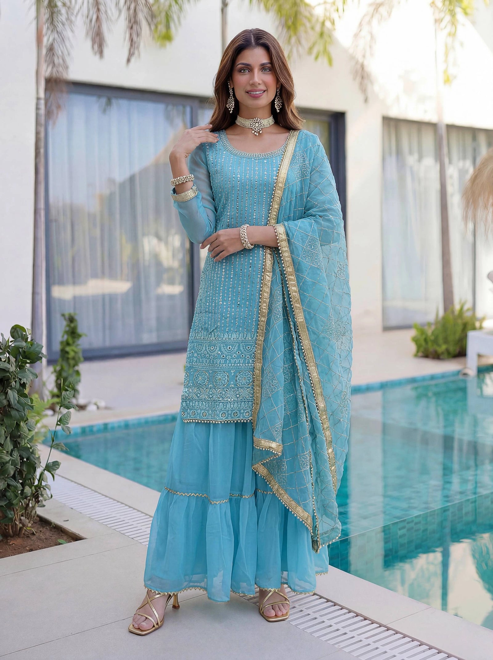 Woman in a light blue traditional outfit standing by a pool.