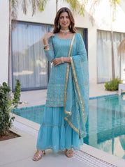 Woman in a light blue traditional outfit standing by a pool.