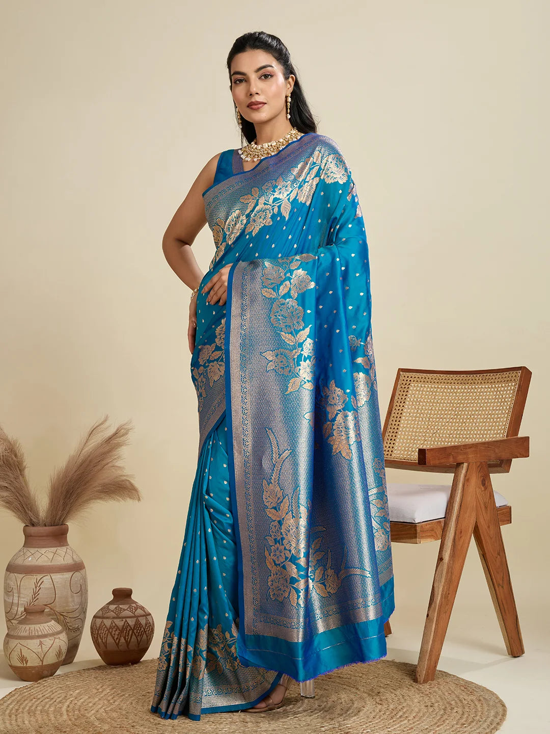 Woman wearing a blue saree with floral patterns in a room setting.