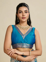 Woman wearing a blue saree with silver border and gold jewelry on a beige background