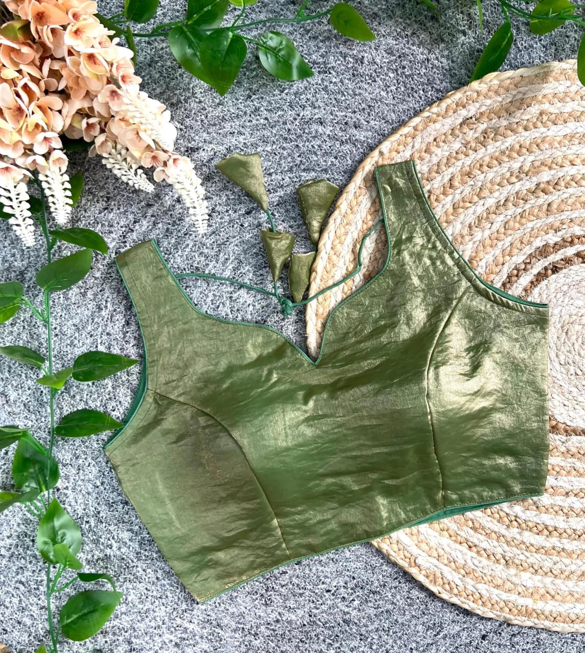 Green satin bralette on a textured surface with floral and woven mat elements.