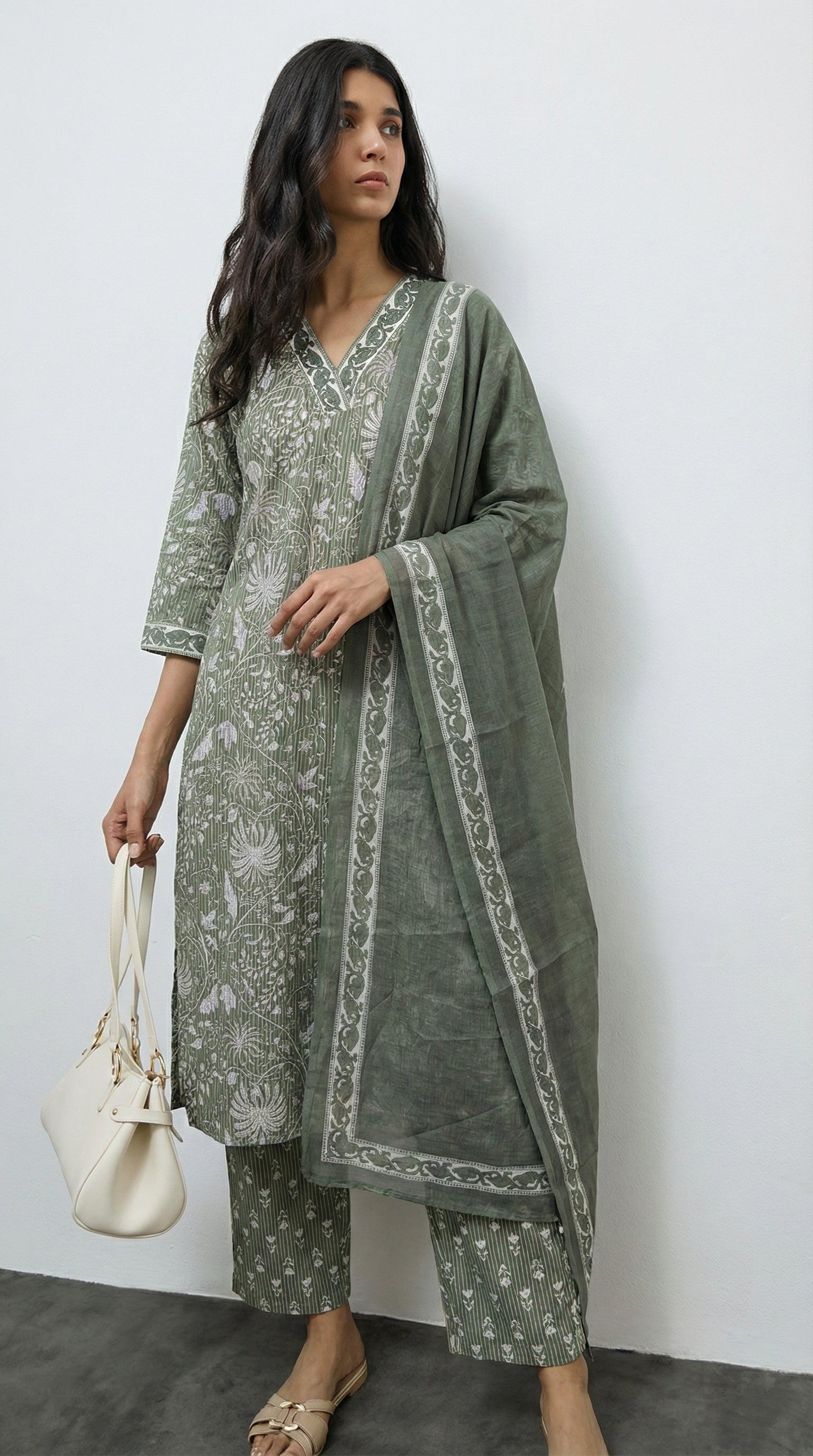 Woman wearing a green traditional outfit with a white pattern against a plain background