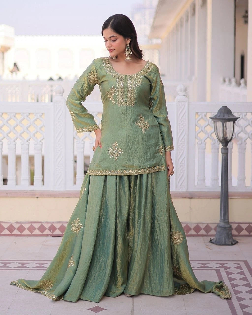 Woman in a green traditional outfit with gold embroidery standing on a patio.