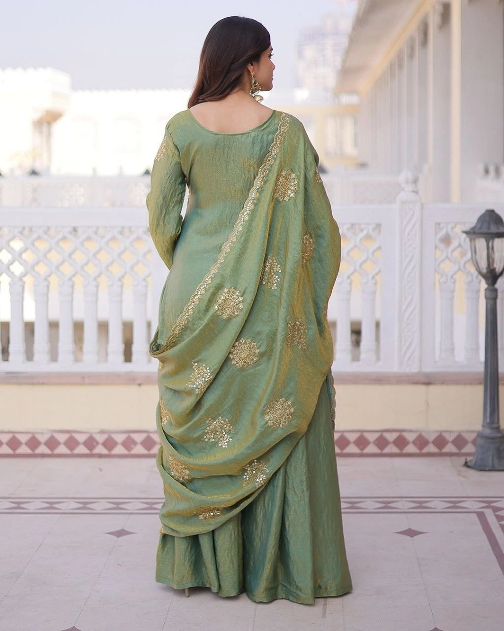 Woman wearing a green saree with gold patterns on a balcony.