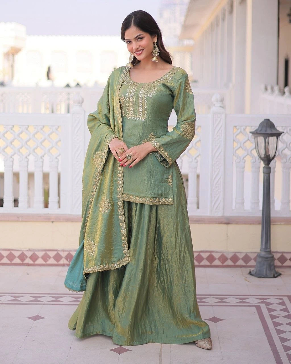 Woman in a green traditional outfit with gold embroidery standing in a decorative indoor setting.