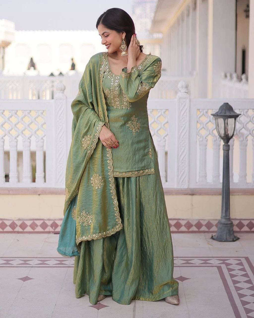 Woman in a green traditional outfit with gold embroidery standing in an outdoor setting.