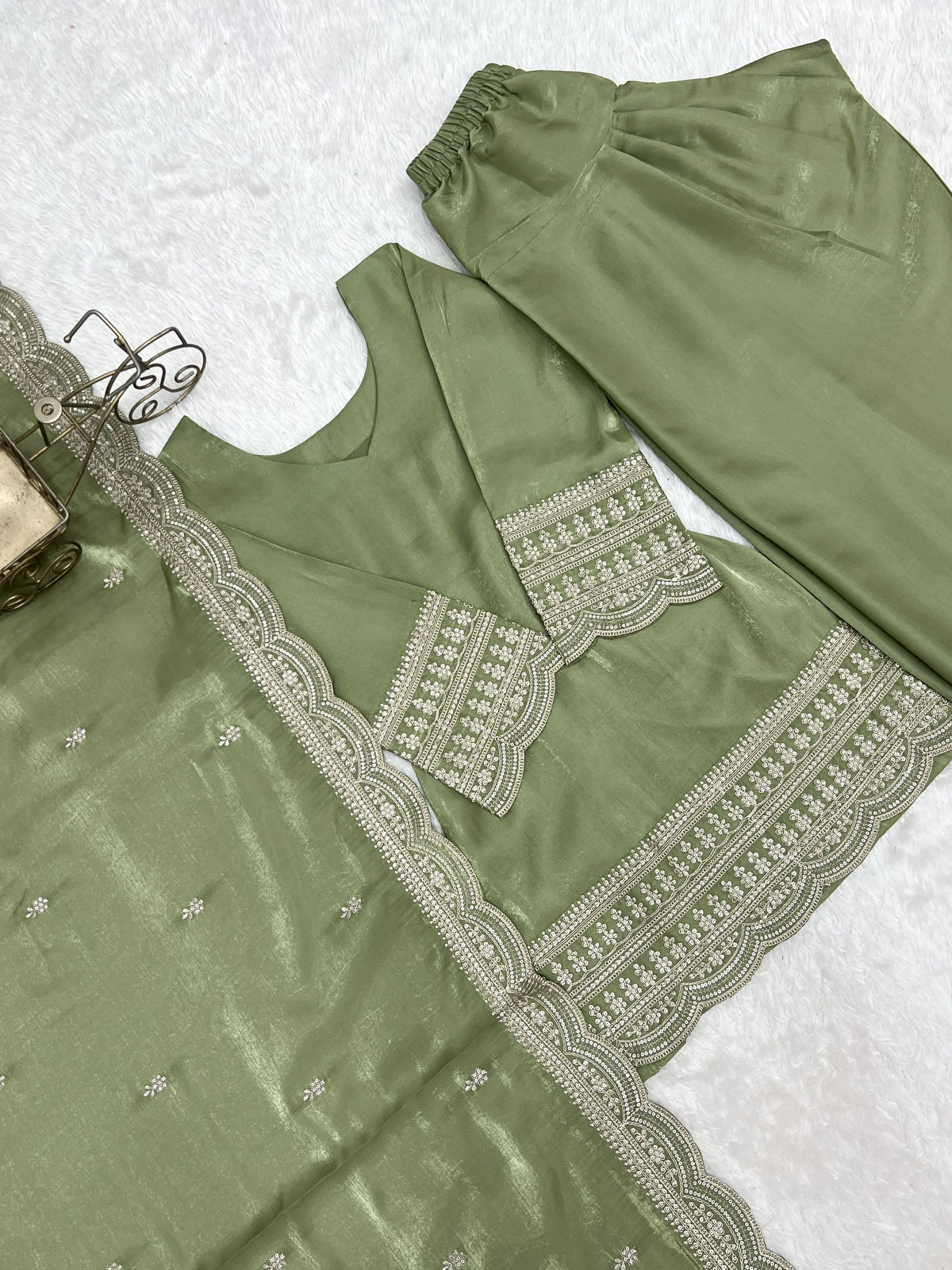 Green traditional outfit with intricate white embroidery on a textured white background