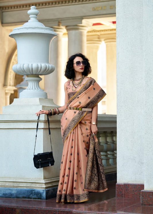 Woman in a peach saree with black patterns standing in front of classical architecture.