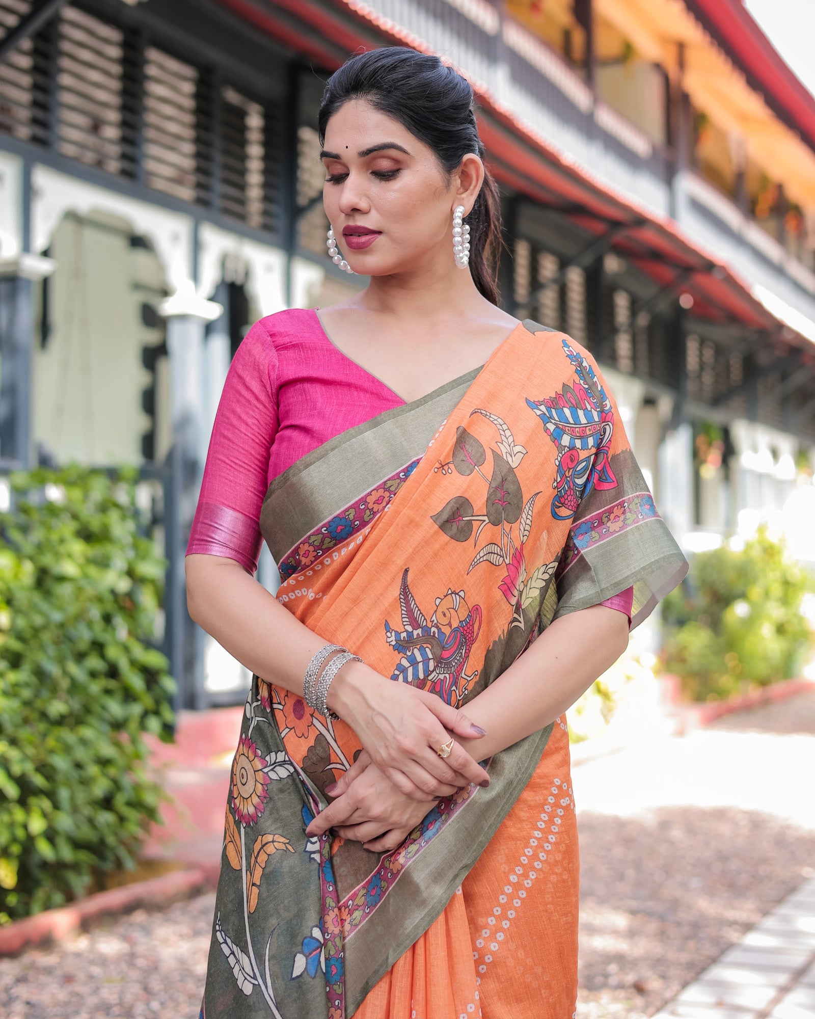 Woman wearing an orange saree with a green border outdoors.