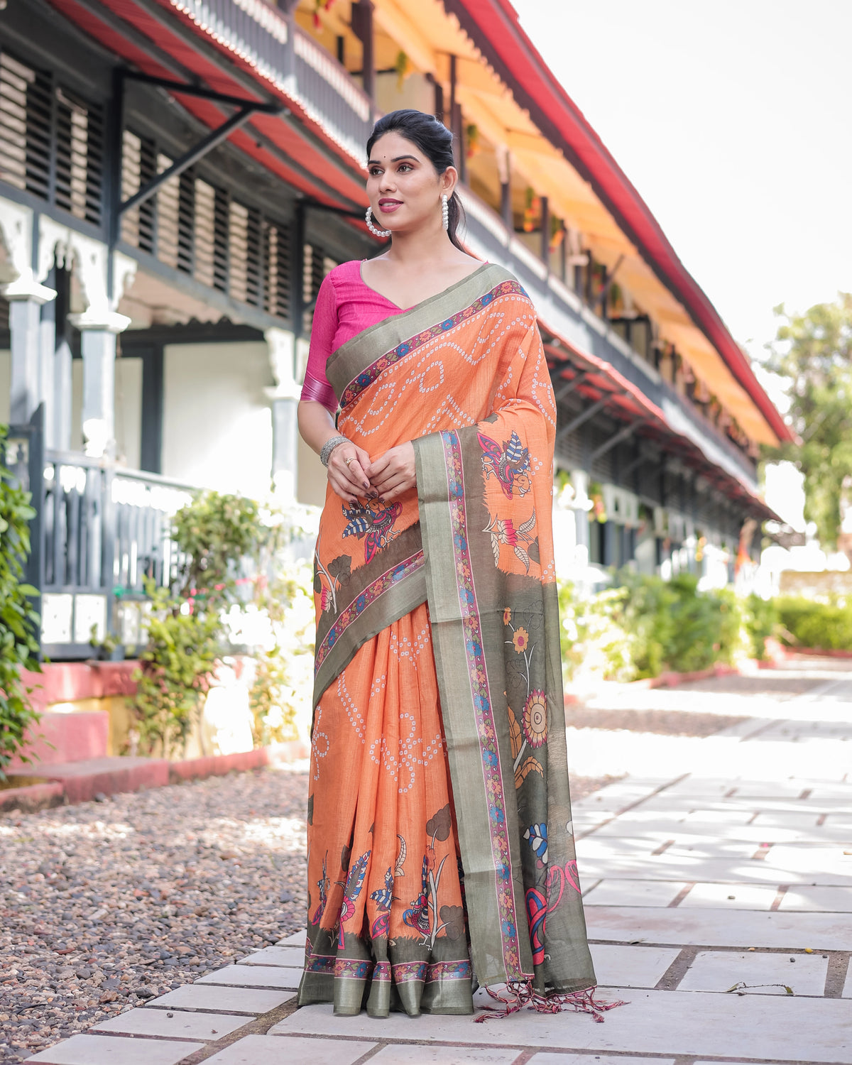 Woman wearing an orange saree with a patterned border in front of a building.