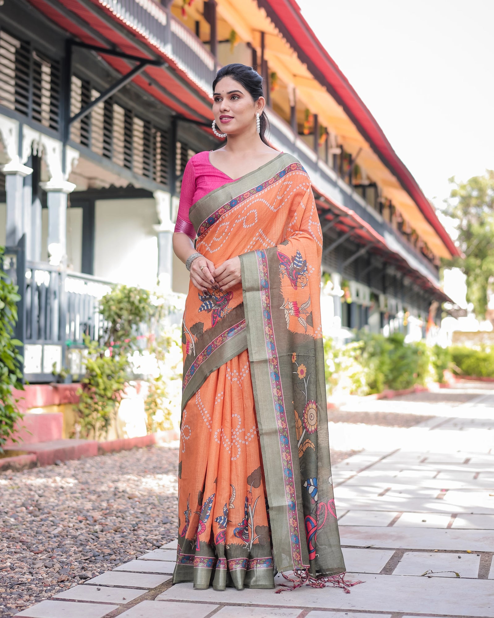 Woman wearing an orange saree with a patterned border in front of a building.