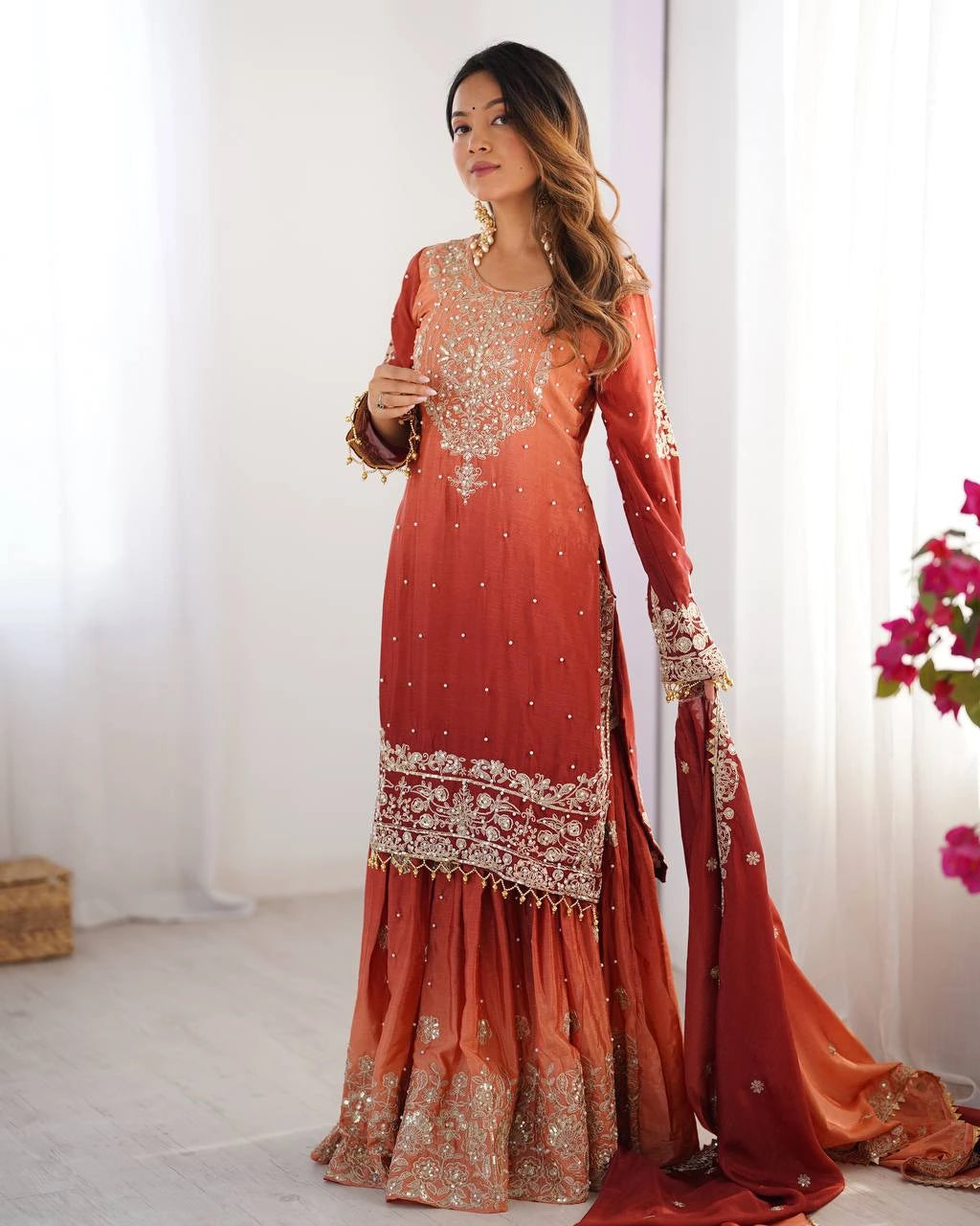 Woman wearing a traditional orange embroidered outfit with a white background