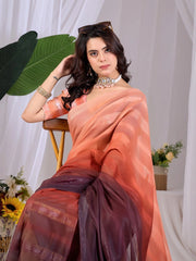 Woman in a peach saree sitting on a chair with a white curtain and decorative elements in the background