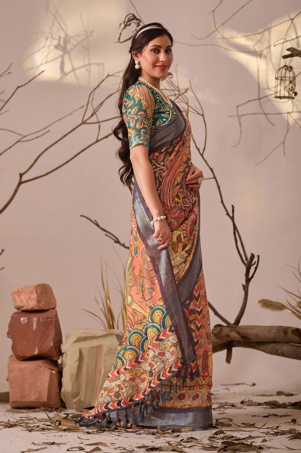 Woman in a colorful traditional outfit standing in a rustic setting with branches and stones.