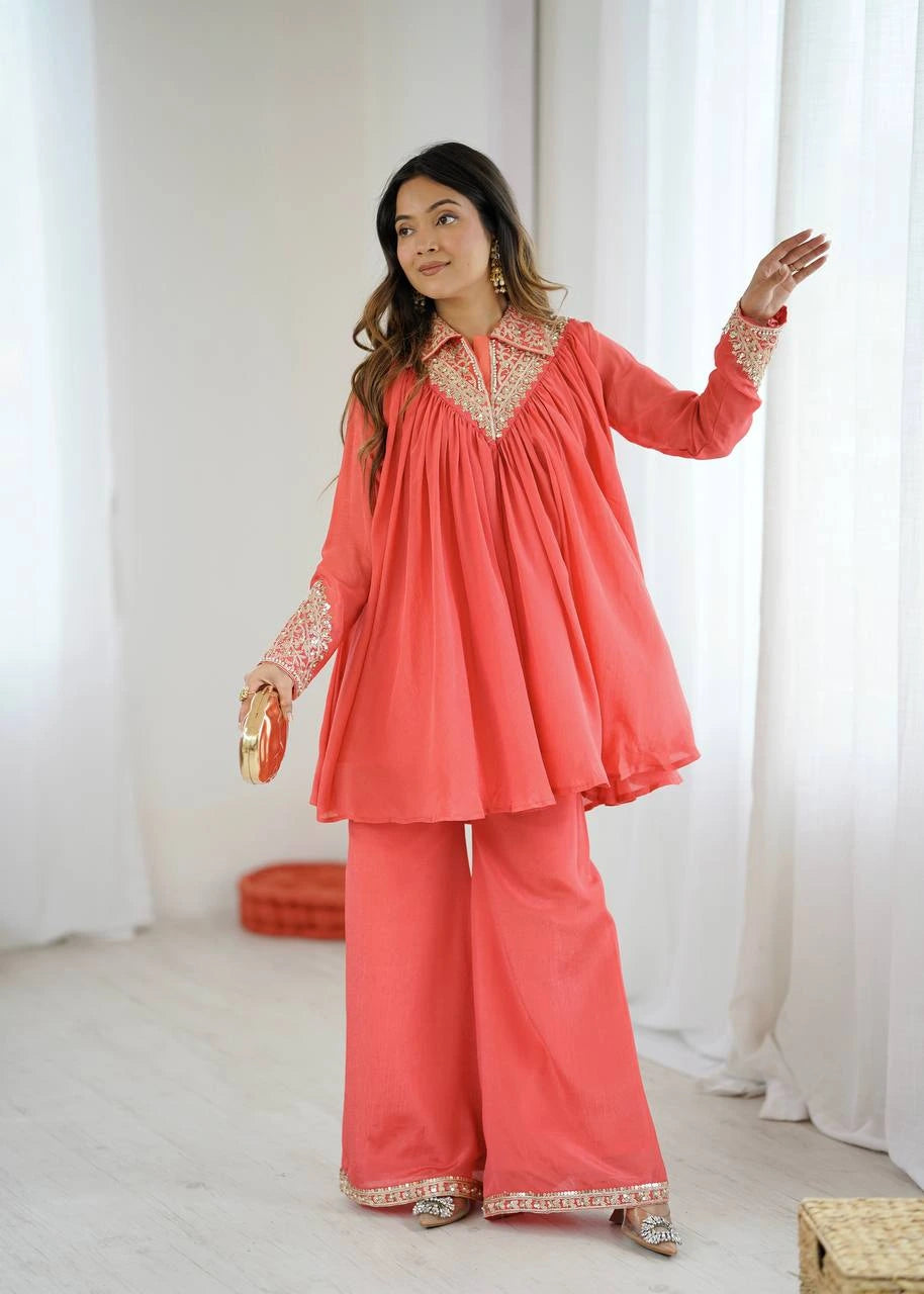 Woman wearing a coral traditional outfit with white embroidery in a bright room.