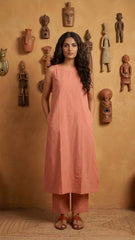 Woman in a peach sleeveless top and pants standing against a wall with decorative masks.