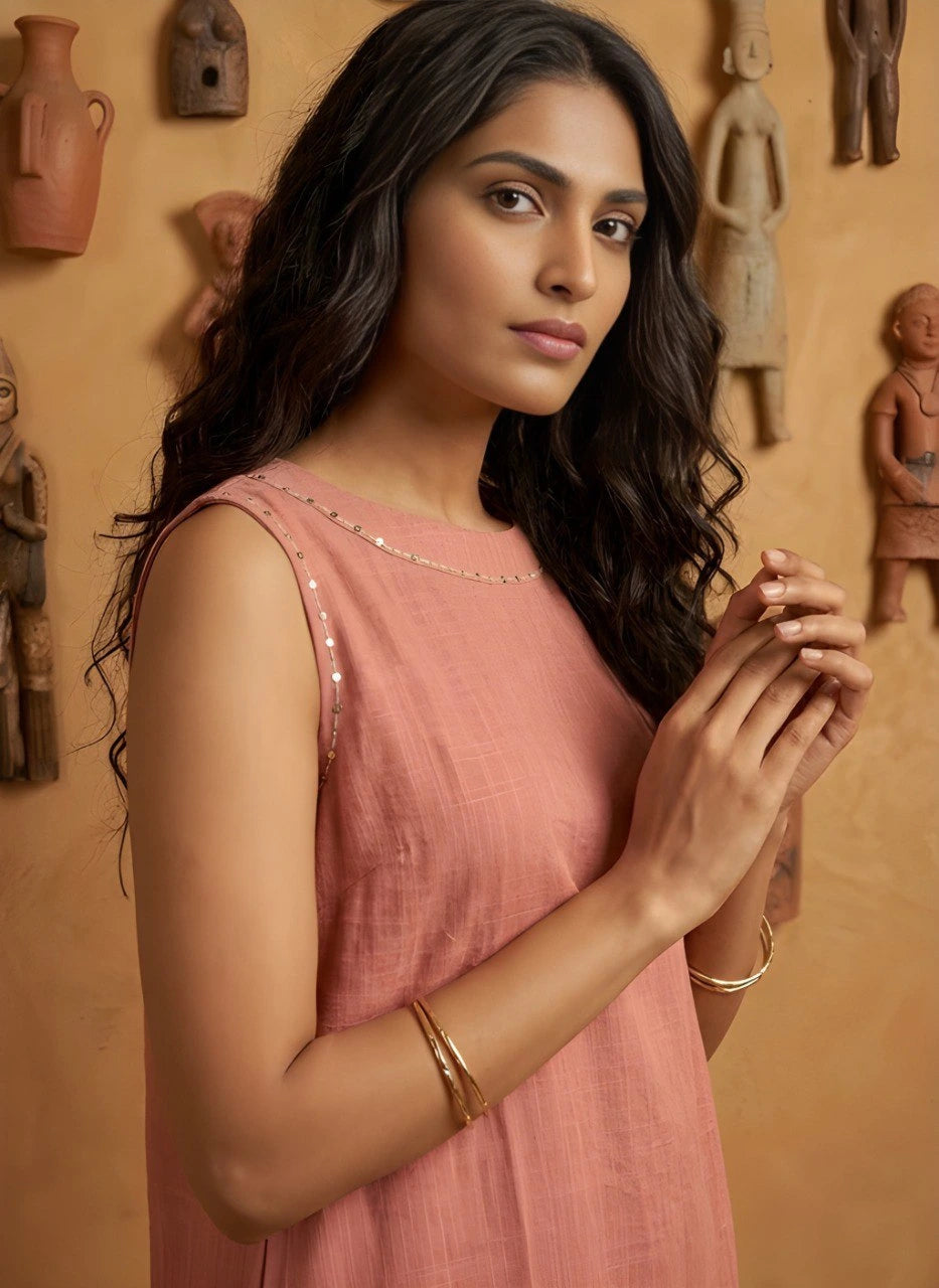 Woman in a pink dress standing against a wall with wooden sculptures.