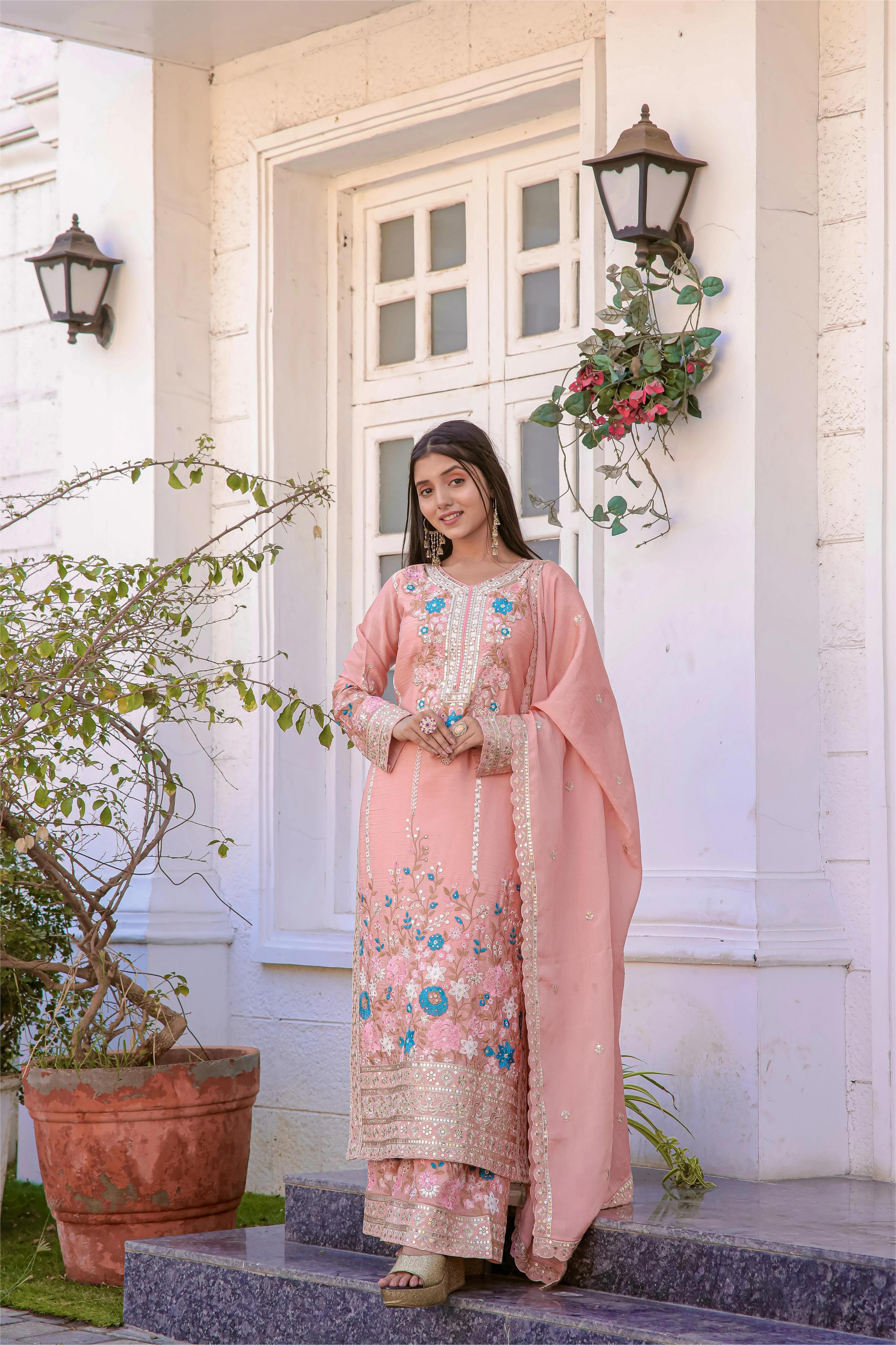 Woman in a pink traditional outfit standing on steps outside a house.
