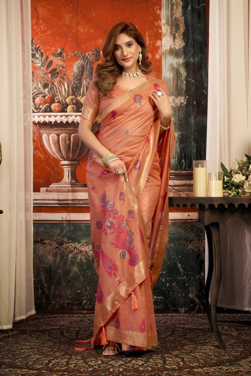 Woman in a peach saree with floral patterns standing in an elegant room.