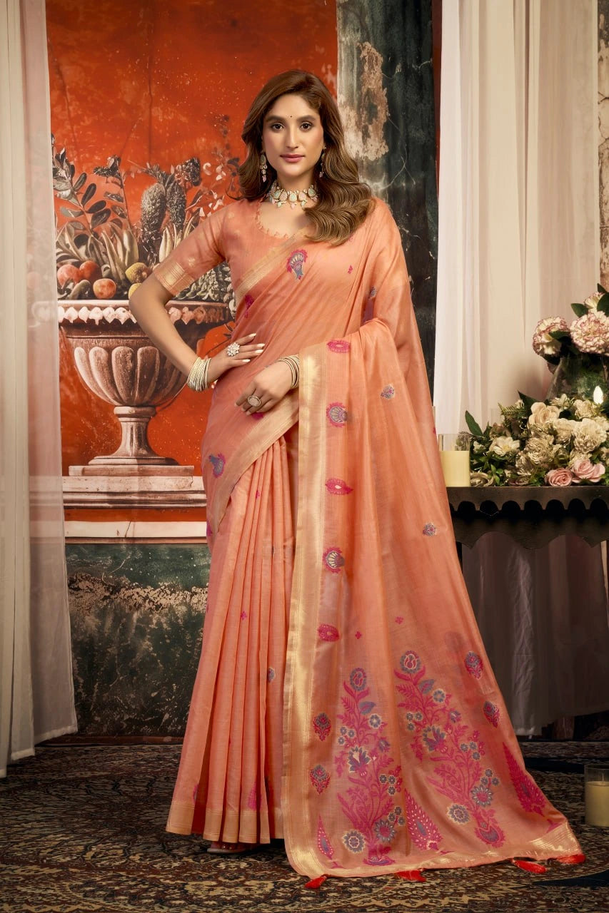 Woman in a peach saree with floral patterns standing in an elegant indoor setting.