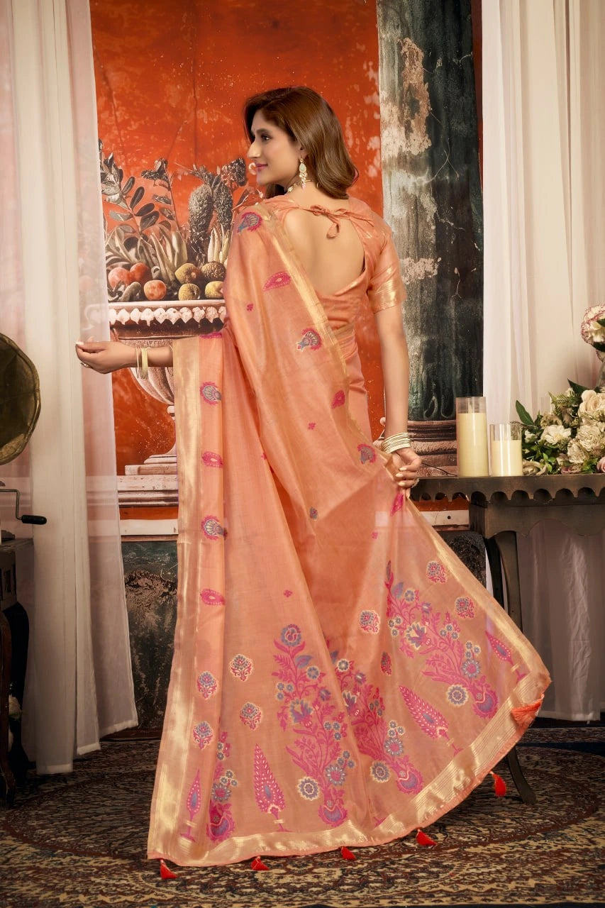 Woman in a peach saree with floral patterns standing indoors.