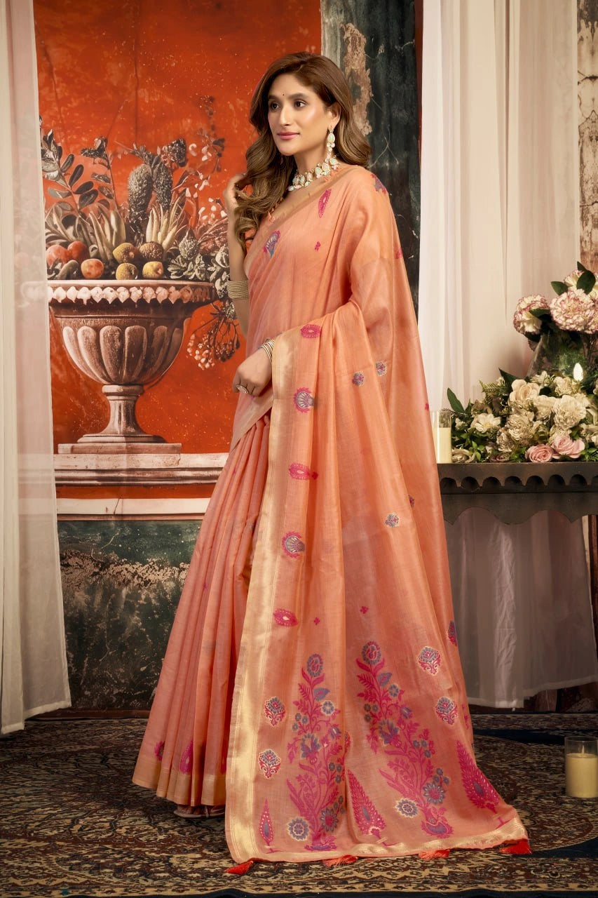 Woman in a peach saree with floral patterns standing in an elegant interior setting.