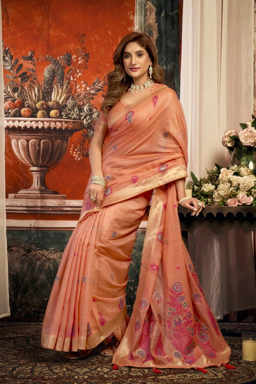 Woman in a peach saree with floral patterns standing in an elegant room.