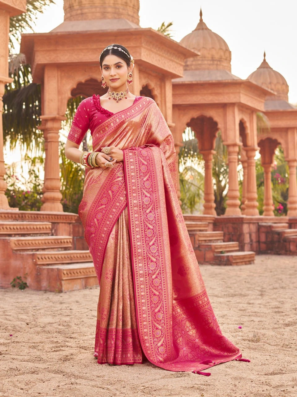 Woman in a traditional pink saree standing in front of an architectural structure.