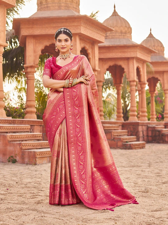Woman in a pink saree standing in front of an architectural structure.