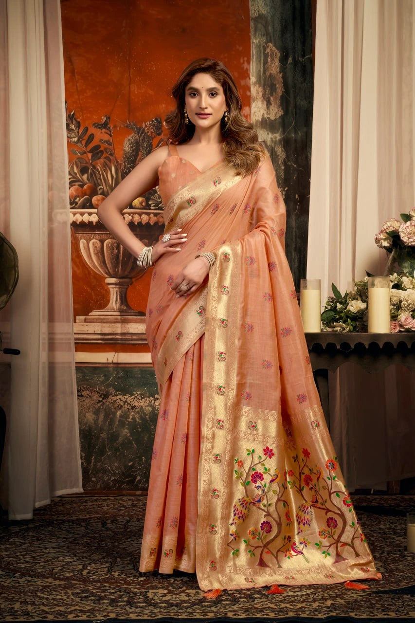 Woman in a peach saree with floral patterns standing in an elegant indoor setting.