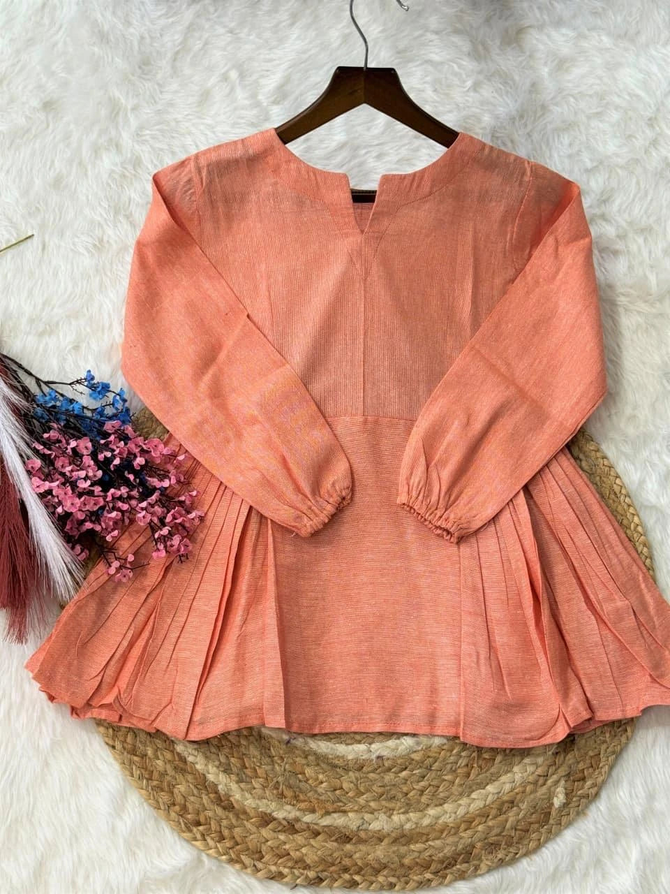 Peach-colored blouse on a hanger with a textured white background
