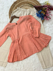 Coral long-sleeve top on a beige hanger with flowers and a hat in the background