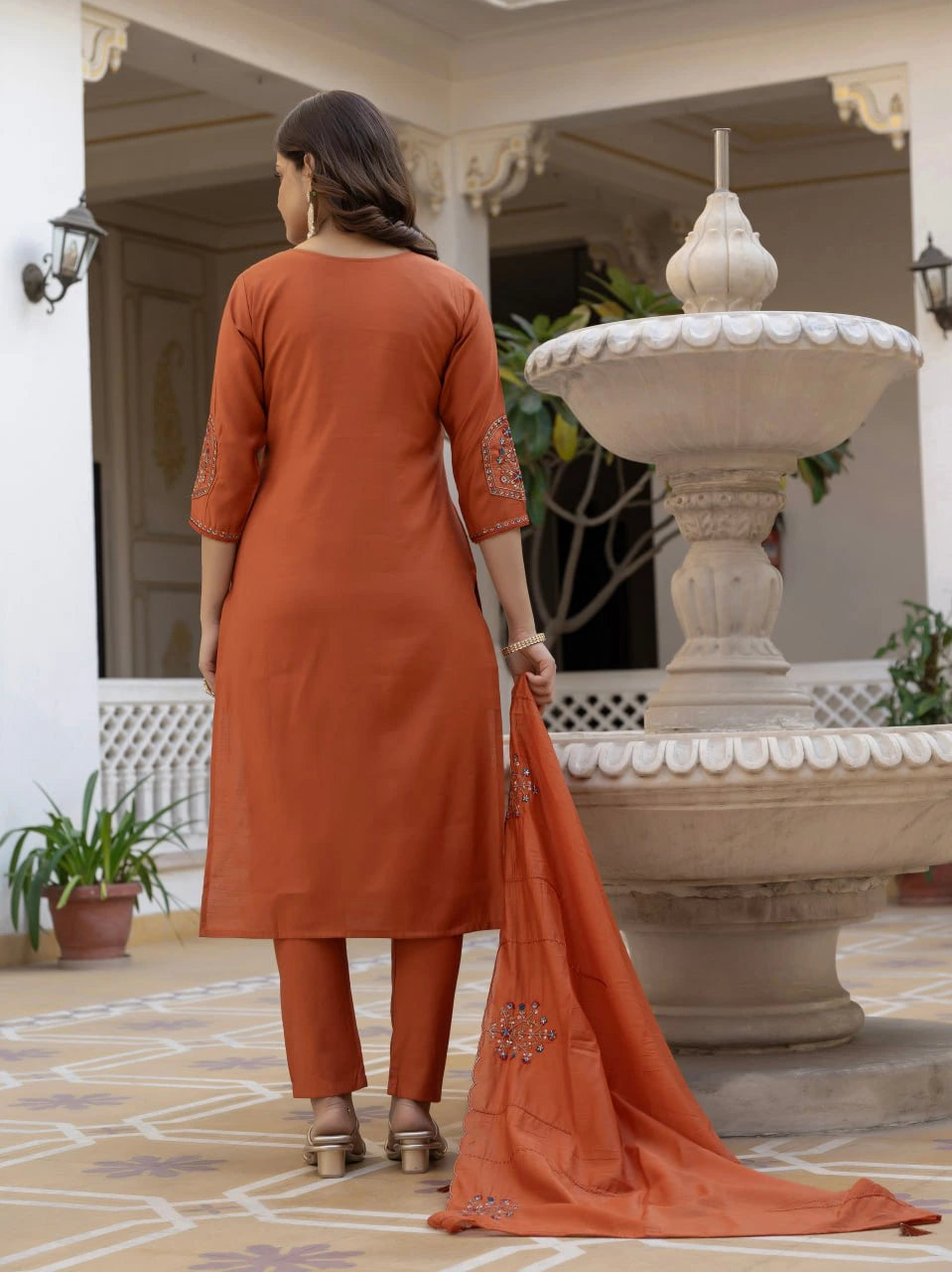 Woman in an orange traditional outfit standing in a decorative outdoor setting.