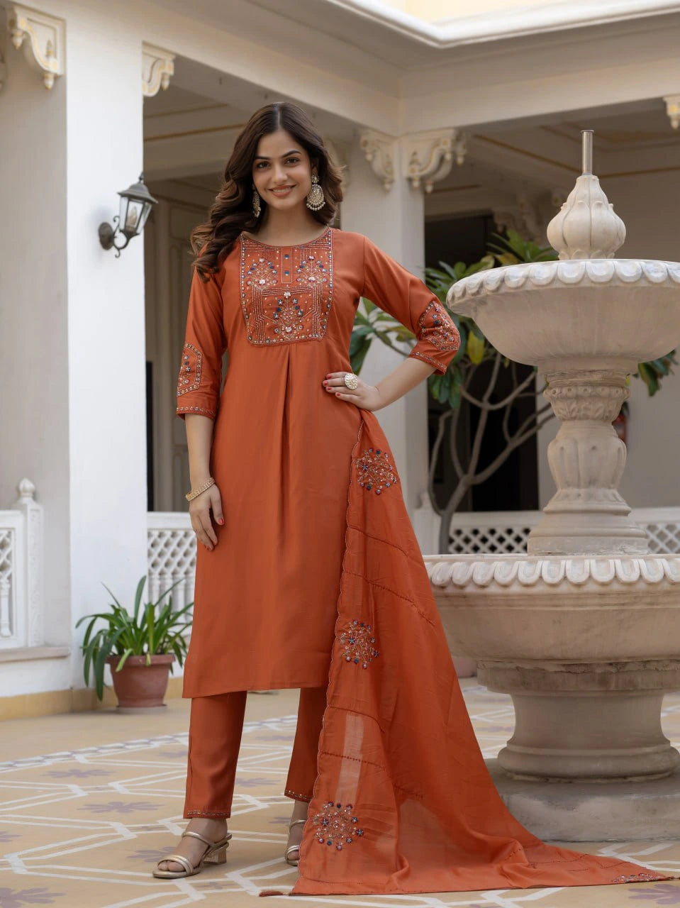 Woman in an orange traditional outfit standing in a decorative indoor setting.