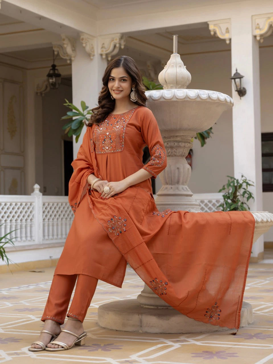 Woman in an orange traditional outfit standing in a decorative indoor setting.