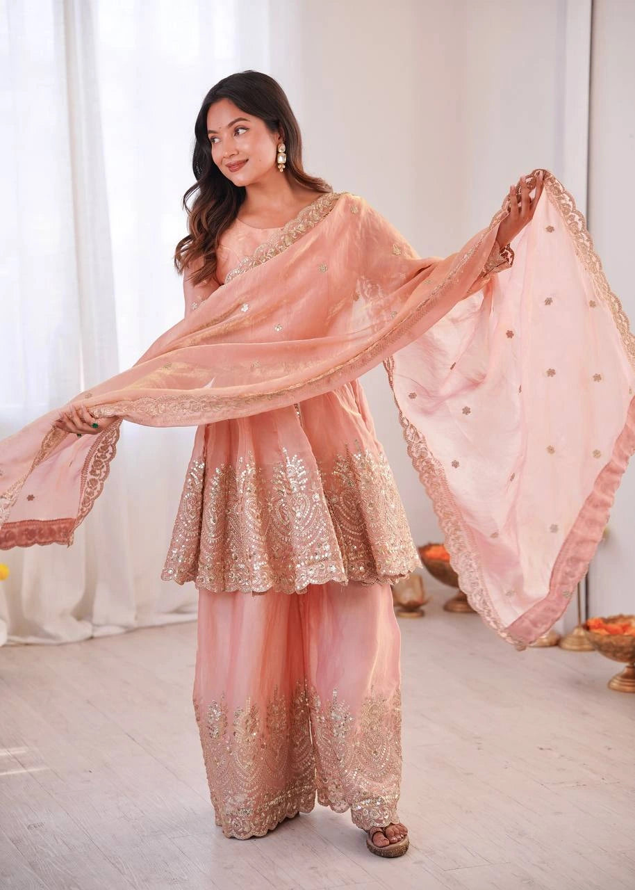 Woman in a peach traditional outfit with a matching dupatta, standing indoors.