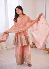 Woman in a peach traditional outfit with a matching dupatta, standing indoors.