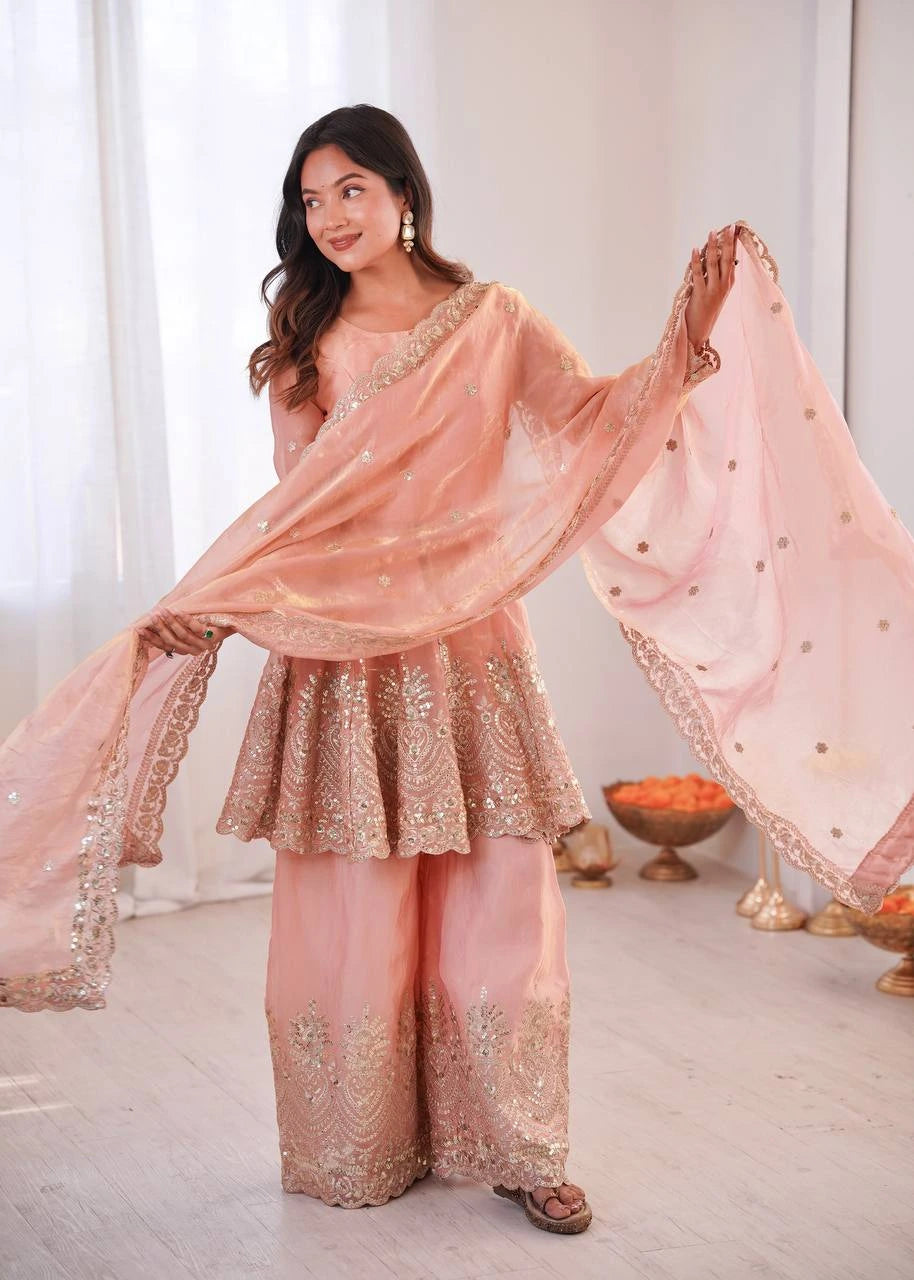 Woman in a traditional outfit with pink and gold colors, standing indoors.