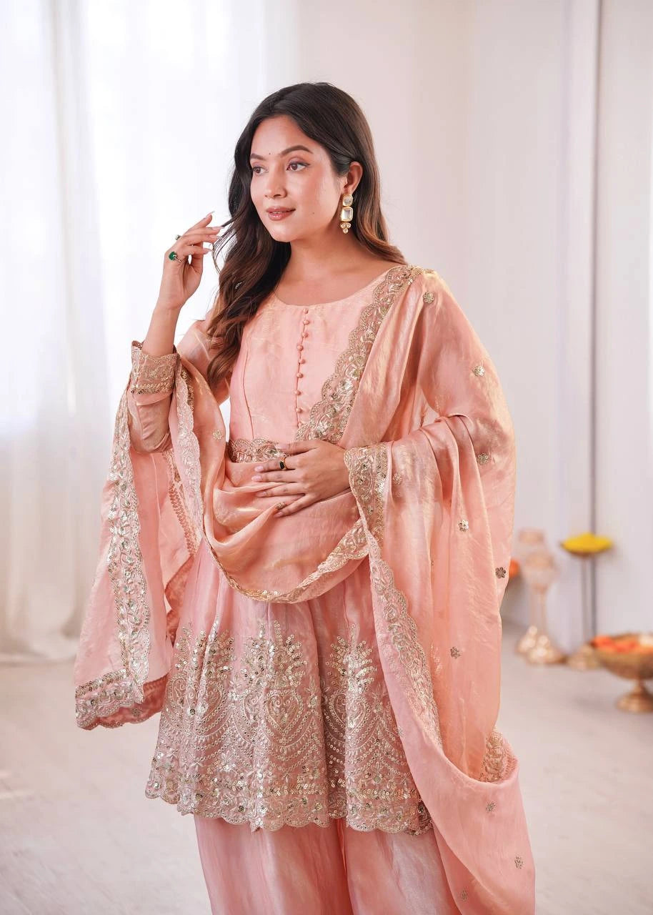 Woman wearing a peach embroidered traditional outfit in a bright room.