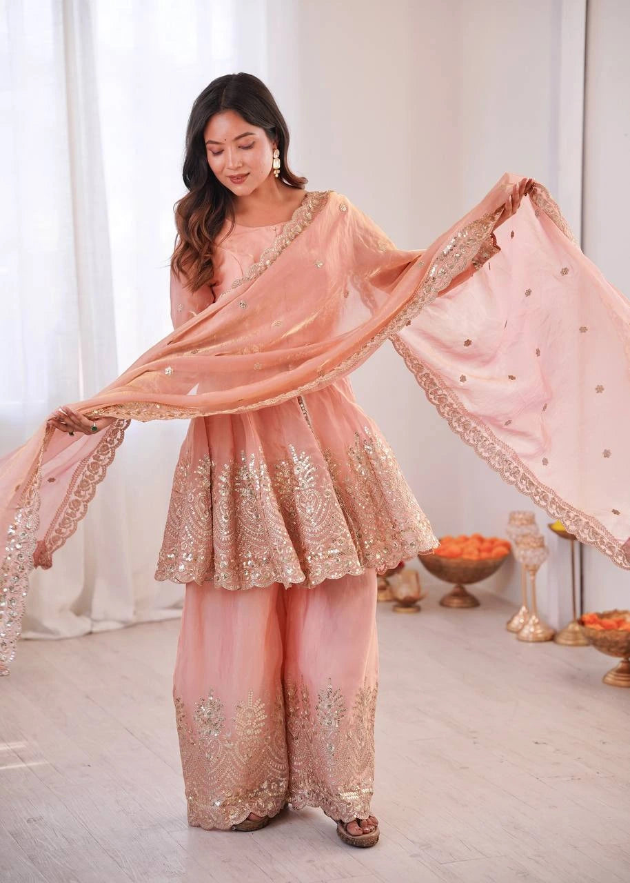 Woman in a traditional pink and gold outfit with a dupatta, standing in a well-lit room.