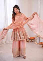 Woman in a traditional pink and gold outfit with a dupatta, standing in a well-lit room.