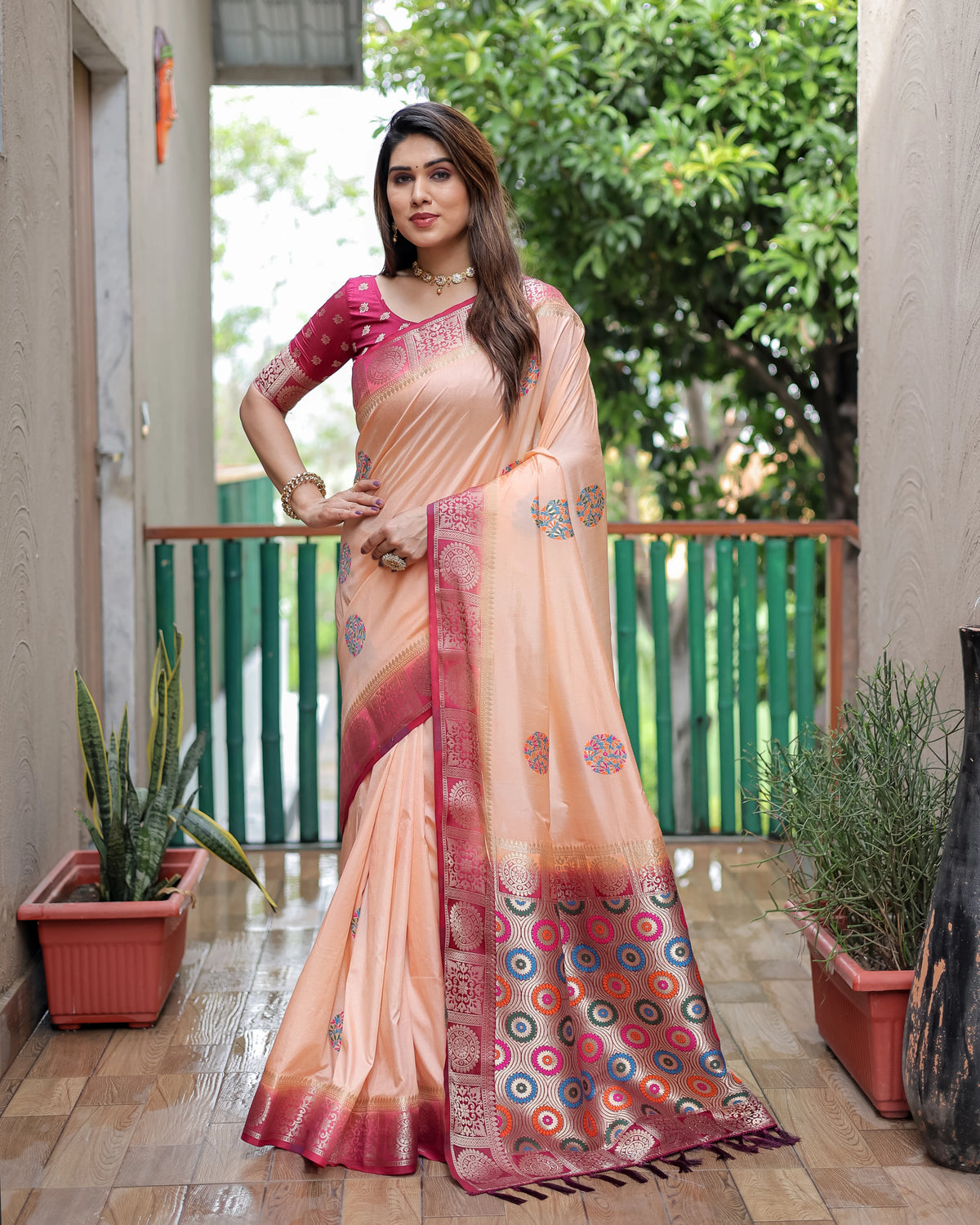 Woman in a peach and pink saree with a colorful border standing outdoors.
