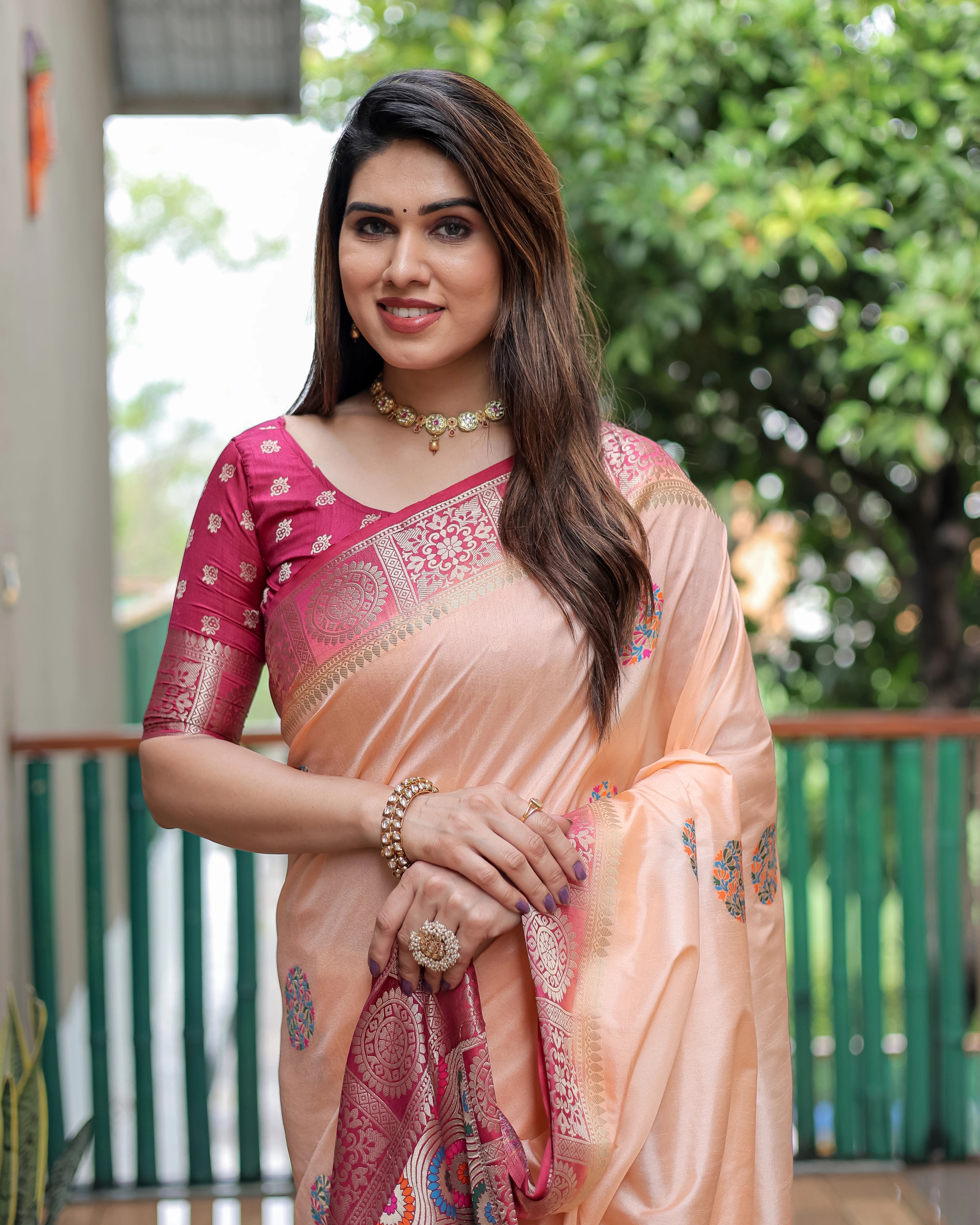 Woman wearing a pink and peach saree with a blurred green background
