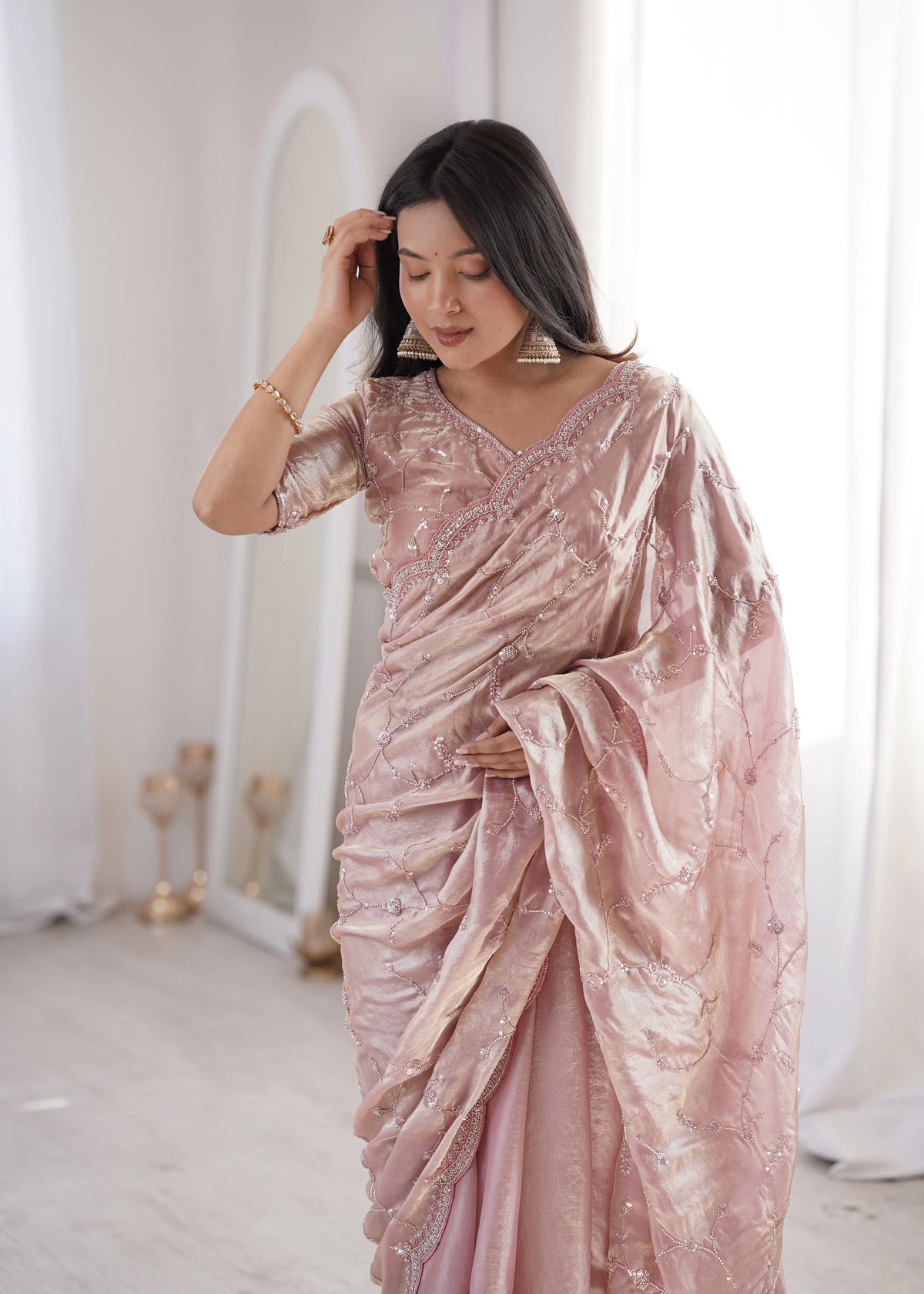 Woman wearing a pink saree with intricate patterns in a minimalistic setting.