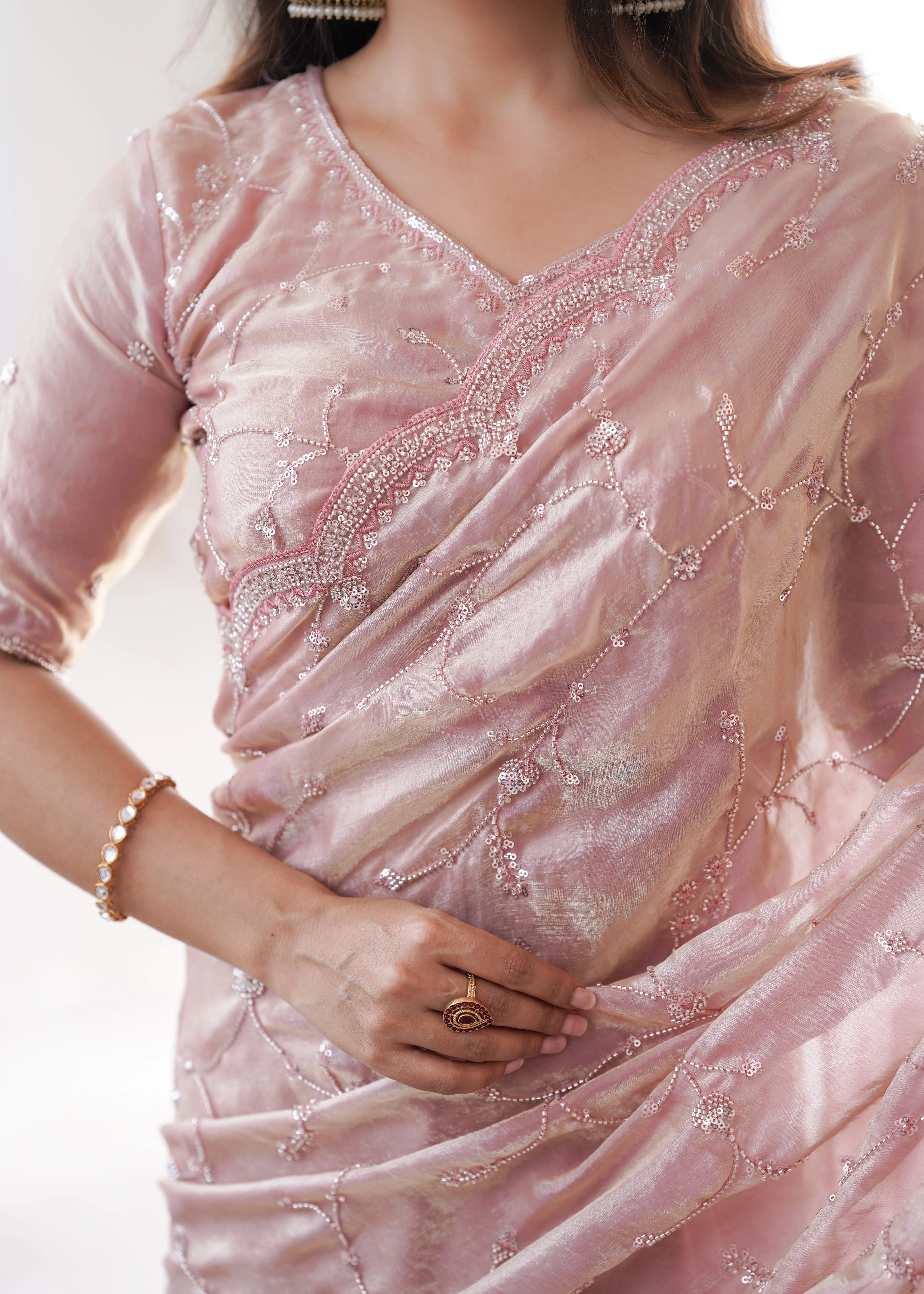 Close-up of a person wearing a pink saree with intricate designs on a plain background