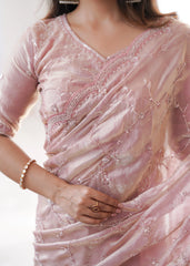 Close-up of a person wearing a pink saree with intricate designs on a plain background