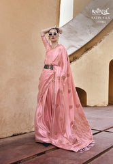 Woman in a pink saree with gold patterns standing against a beige wall.
